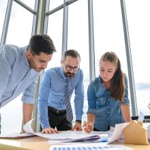 Tres personas vistas apoyadas en una mesa de reuniones mientras se informan sobre las Directivas de Grupo (GPO).