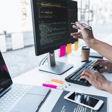 Un hombre apunta a la pantalla de un ordenador mientras otro pulsa el teclado, durante una auditor&iacute;a de software.