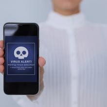 Esku batek mugikor bat erakusten du, eta haren pantailan birus-alerta bat agertzen da.