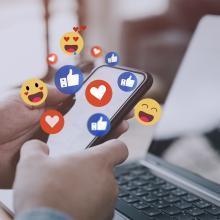 Las manos de un hombre sujetan un m&oacute;vil rodeado de emojis, representando las buenas pr&aacute;cticas en redes sociales.