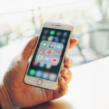 Una mano sostiene un m&oacute;vil en cuya pantalla aparecen diversos iconos de aplicaciones, que representa la gesti&oacute;n del riesgo en redes sociales.