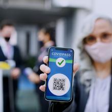 Emakume batek mugikor bat erakusten du, eta haren pantailan COVID-19aren eta txertaketaren inguruko iruzurrei buruzko informazioa agertzen da.