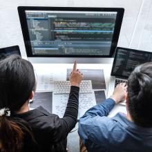 Dos personas que trabajan en el SOC - (Centro de Operaciones de Seguridad), frente a la pantalla de un ordenador.