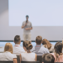 Un hombre con un micr&oacute;fono hablando ante una audiencia sobre formaci&oacute;n y concienciaci&oacute;n en ciberseguridad.