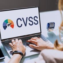 Gizon baten eskuak ordenagailu eramangarri baten teklatuaren gainean. Haren pantailan CVSS siglak agertzen dira.