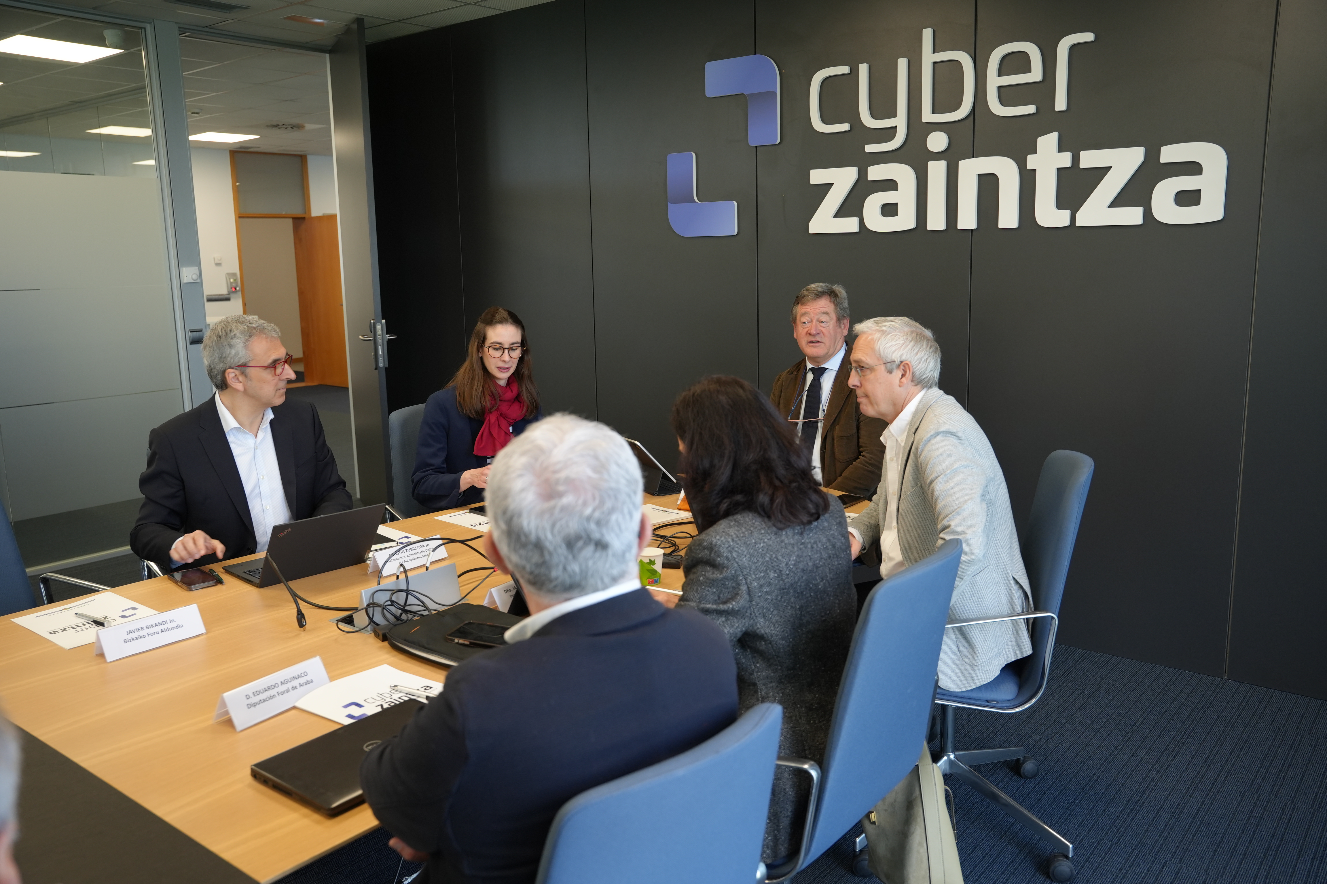Foto de un momento de la reuni�n del Consejo de Administraci�n de Cyberzaintza, en el que varios de los participantes se encuentran sentados en la mesa de reuniones de la Agencia Vasca de Ciberseguridad.