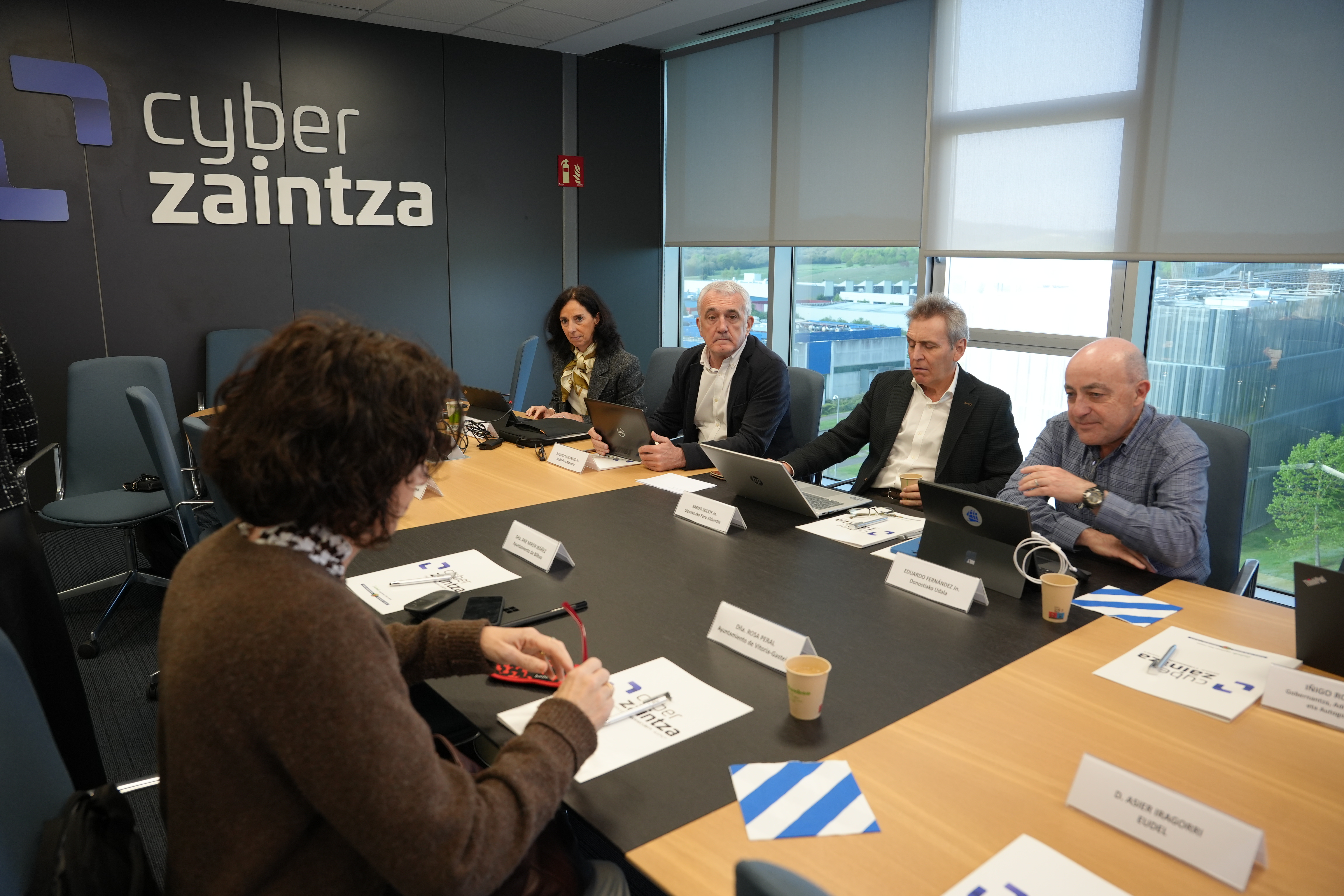 Foto de un momento de la reuni�n del Consejo de Administraci�n de Cyberzaintza, en el que varios de los participantes se encuentran sentados en la mesa de reuniones de la Agencia Vasca de Ciberseguridad.