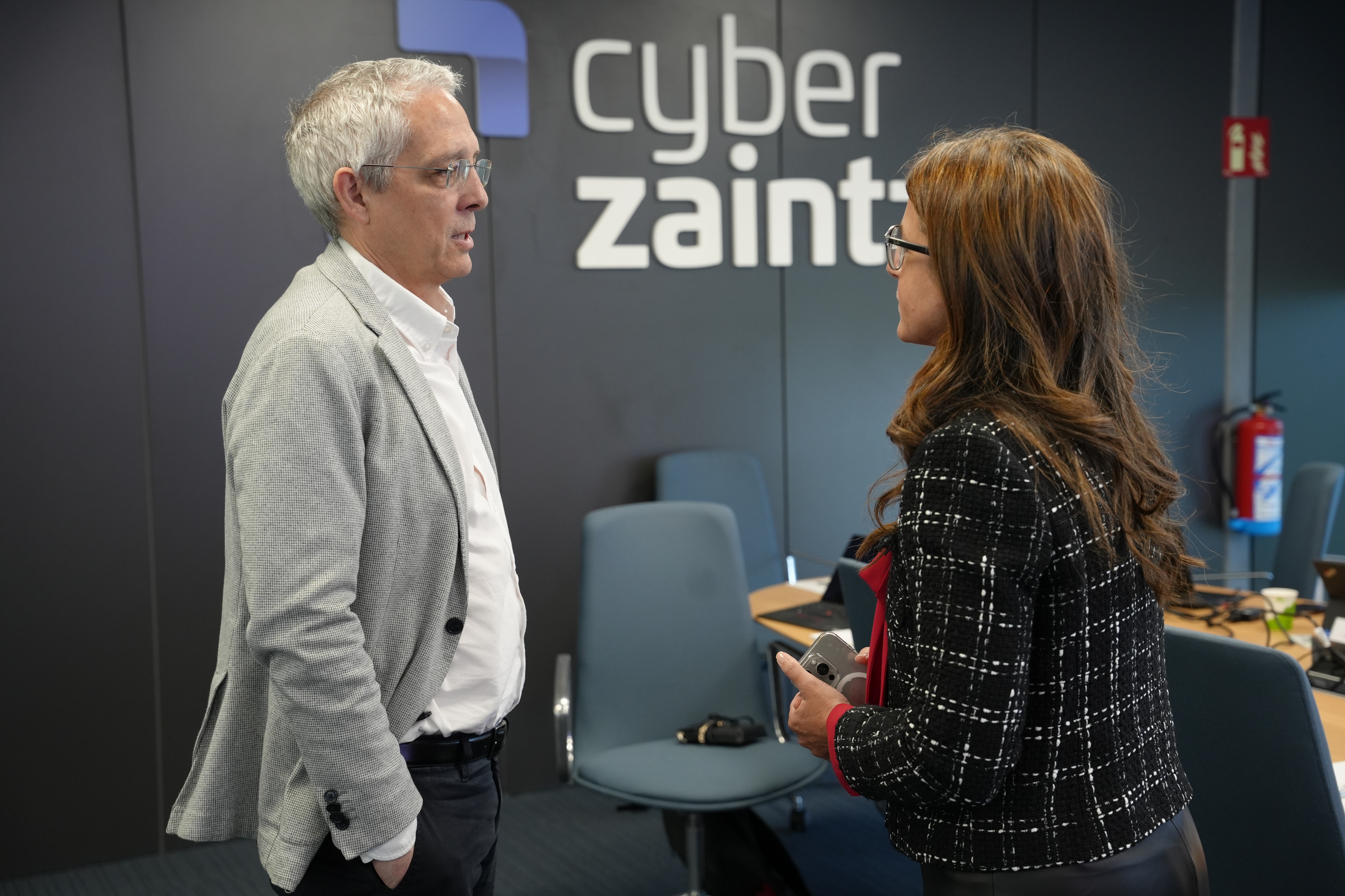 Foto de un momento de la reuni�n del Consejo de Administraci�n de Cyberzaintza, en el que dos participantes se ven de pie en la sala de reuniones de la Agencia Vasca de Ciberseguridad.