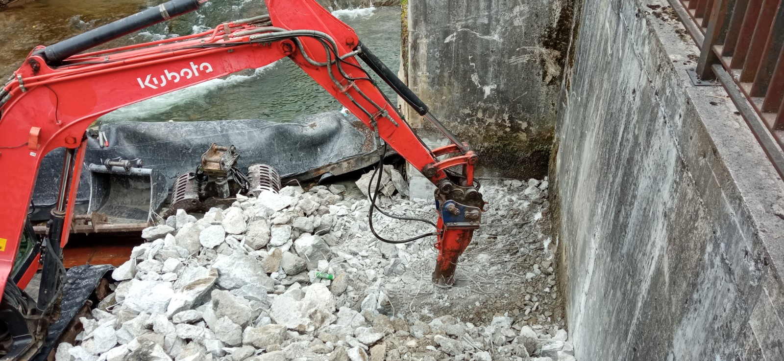 Excavadora picando la base y el estribo de la presa